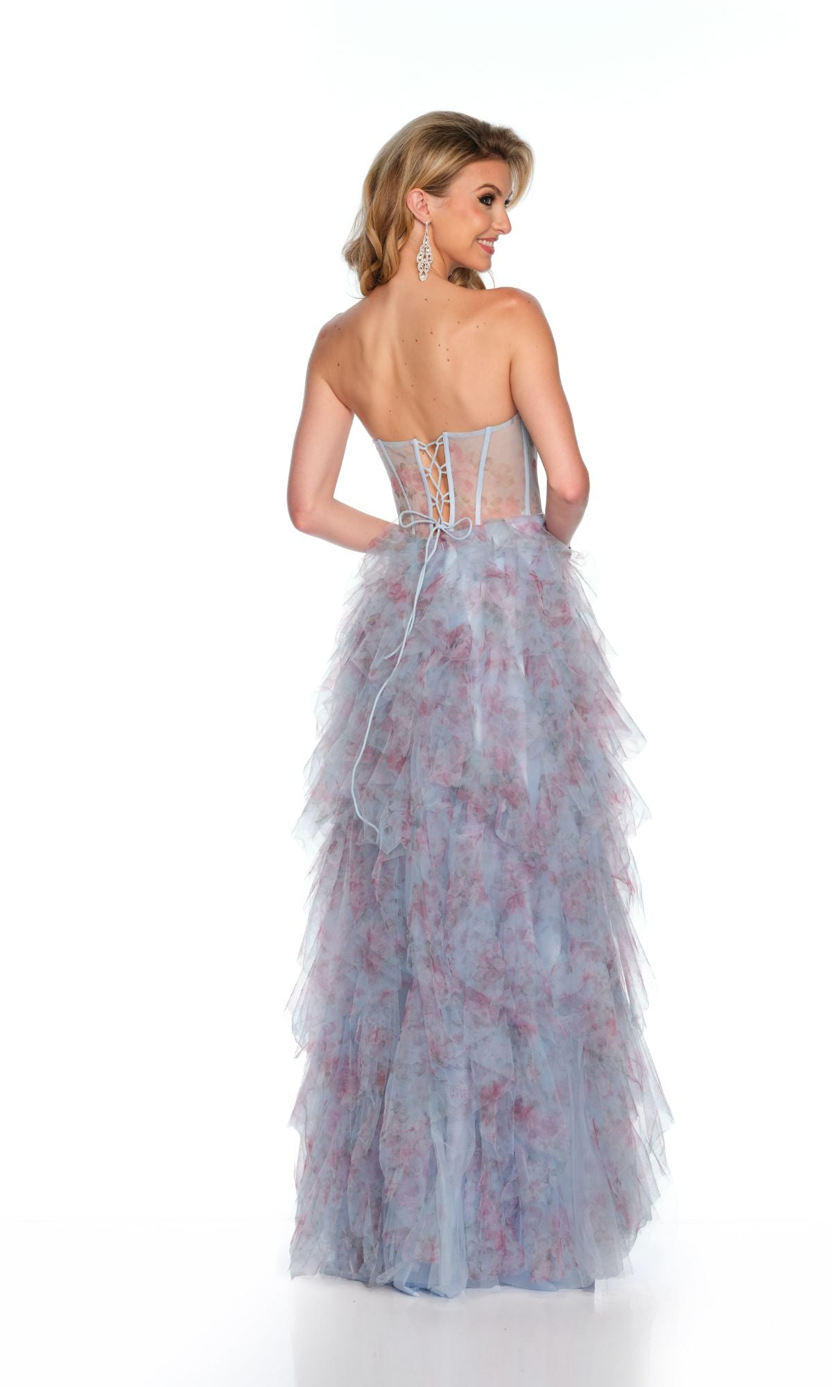 A woman stands facing away from the camera in the Long Formal Dress 11636 by Dave and Johnny, a strapless print gown with a sheer boned bodice, blue and pink ruffles, and a lace-up back.
